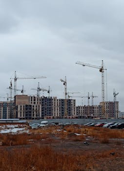 Construction cranes at a building site in Ekibastuz, Kazakhstan under a cloudy sky.