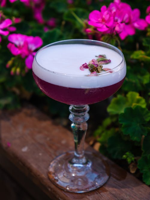 A Cocktail Drink with Pink Flowers Floating on Foam