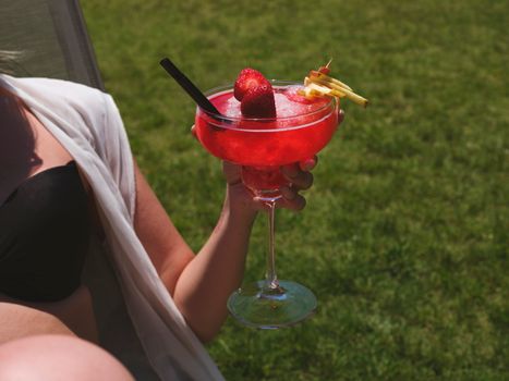 Enjoy a refreshing strawberry cocktail outdoors on a sunny day. Perfect for summer relaxation.