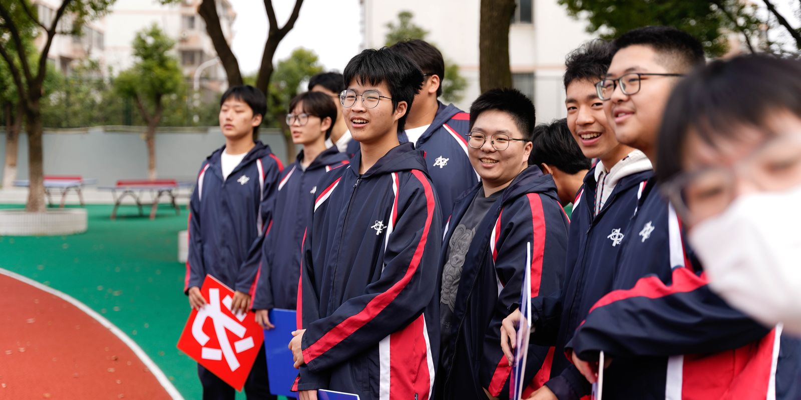 A group of smiling Asian high school students outdoors in Wuxi, Jiangsu, China, wearing school uniforms.
