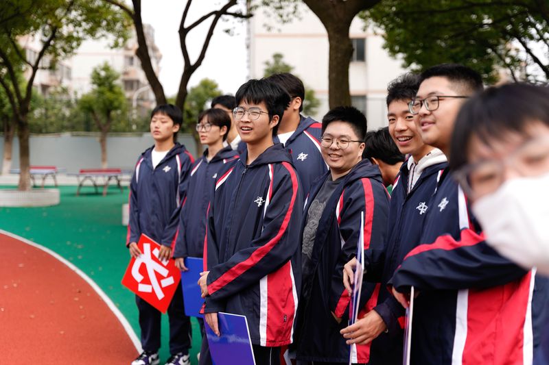 A group of smiling Asian high school students outdoors in Wuxi, Jiangsu, China, wearing school uniforms.
