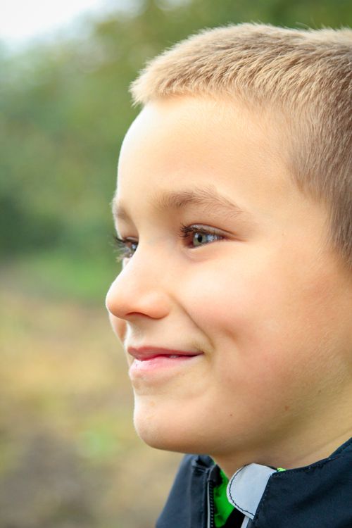 Free A close-up profile of a smiling boy with a blurred outdoor background. Stock Photo