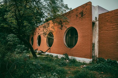 Free A rustic building with circular windows surrounded by lush greenery, showcasing architectural innovation. Stock Photo
