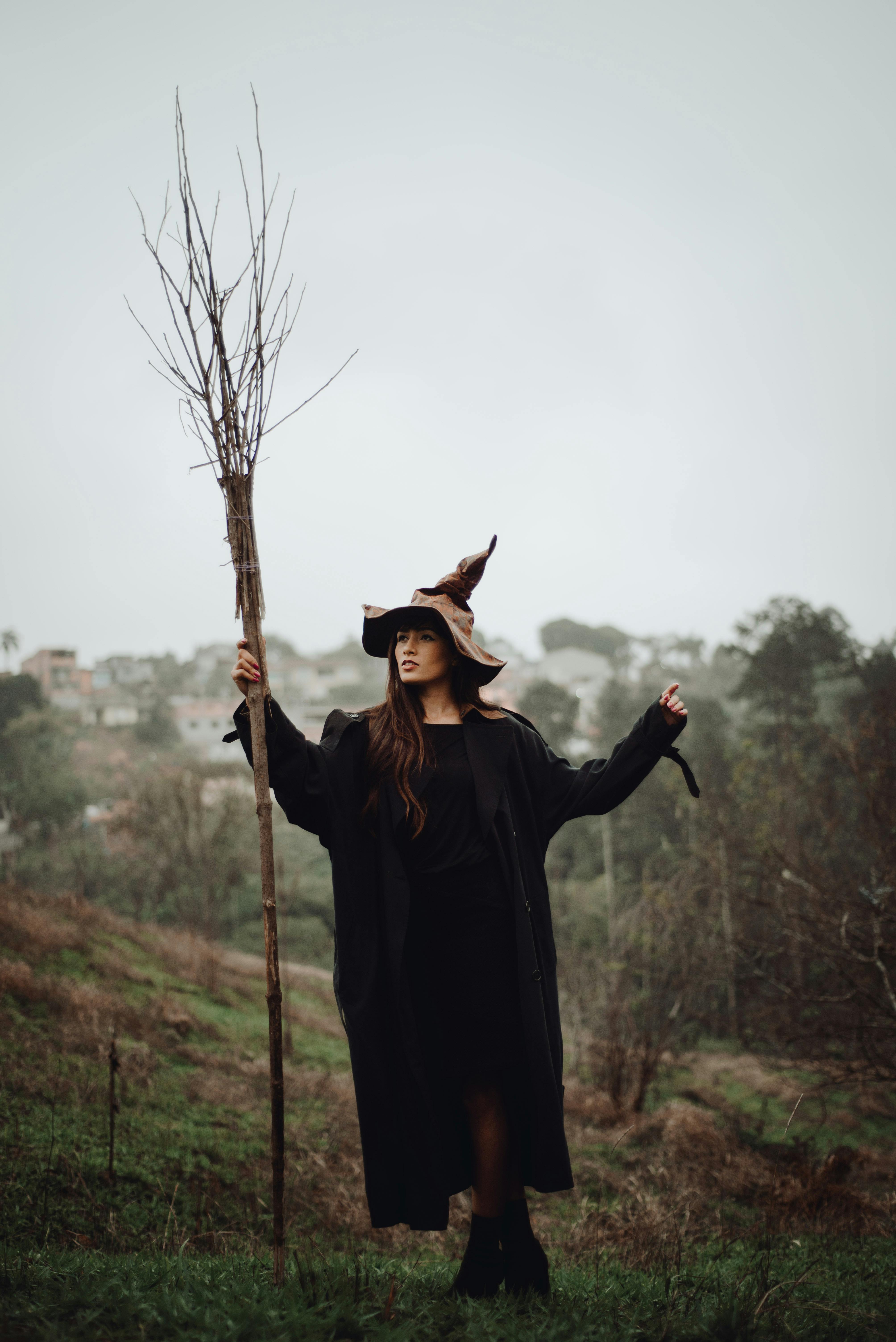 A mysterious woman in a witch costume stands outdoors, creating a spooky Halloween vibe.