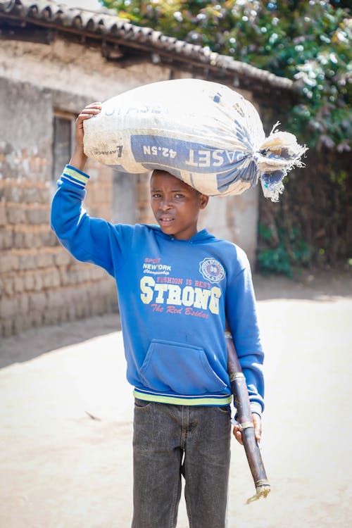 Boy in Blue Hoodie Carrying a Sack on Head