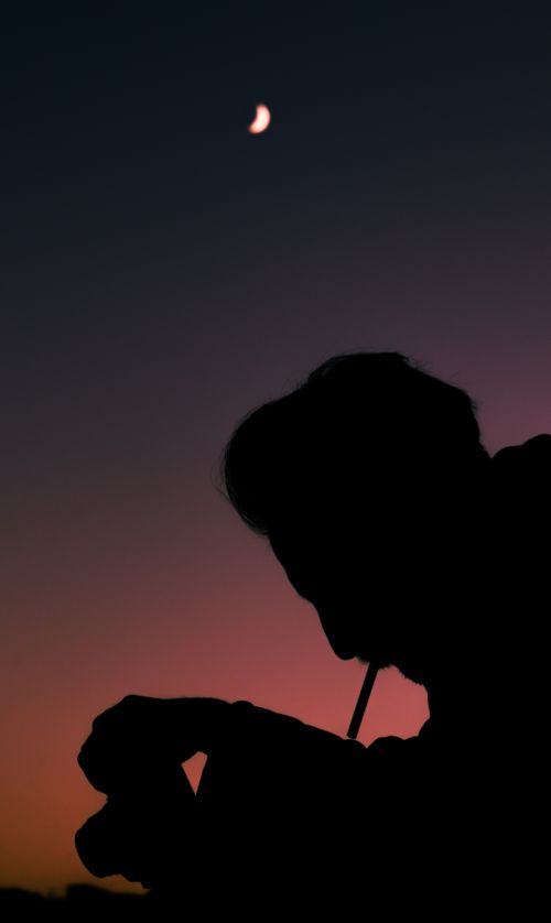 Free A silhouetted person smoking under a night sky with a visible moon crescent. Stock Photo