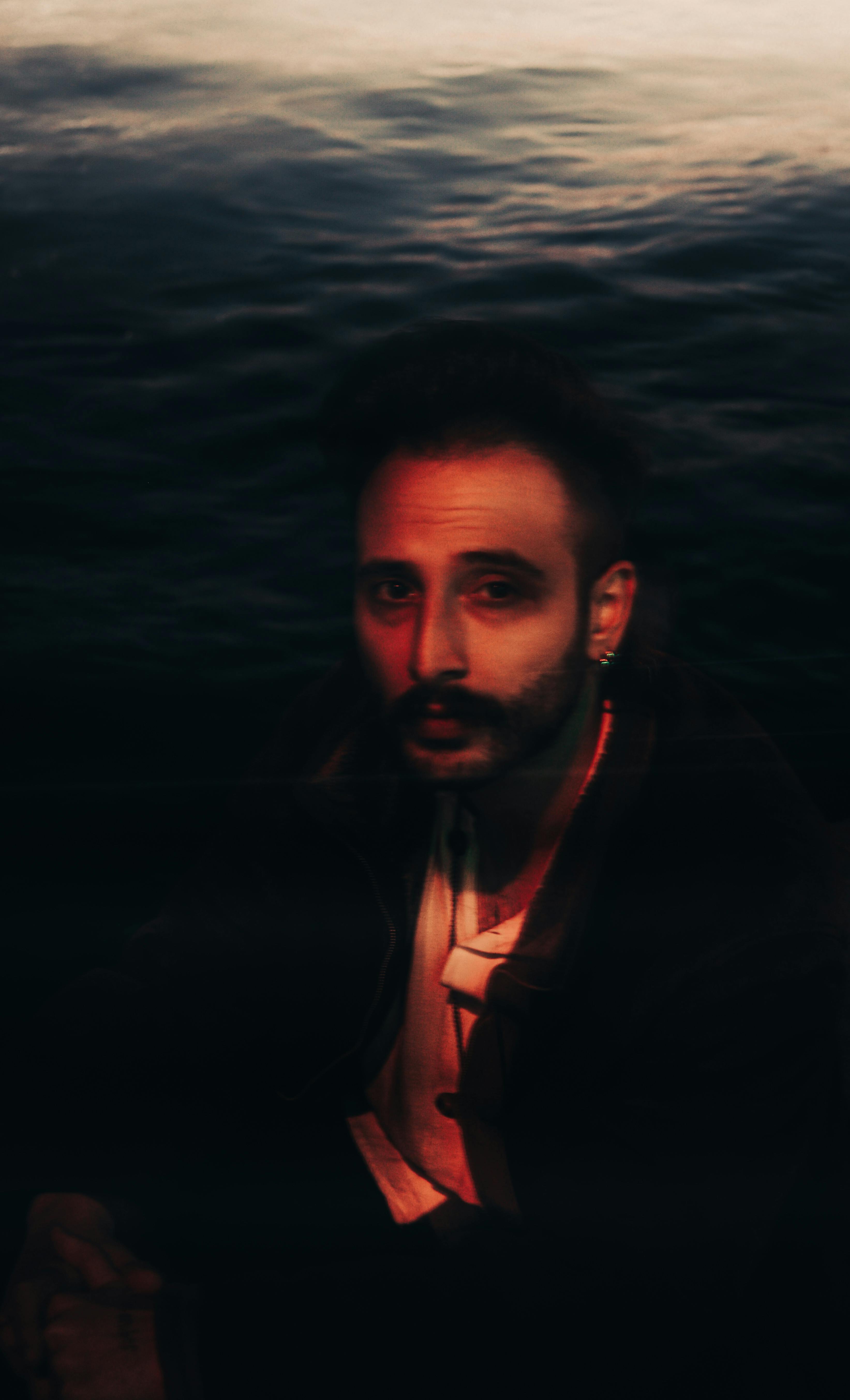 A mysterious portrait of a bearded man with moody lighting by the sea, taken at night.
