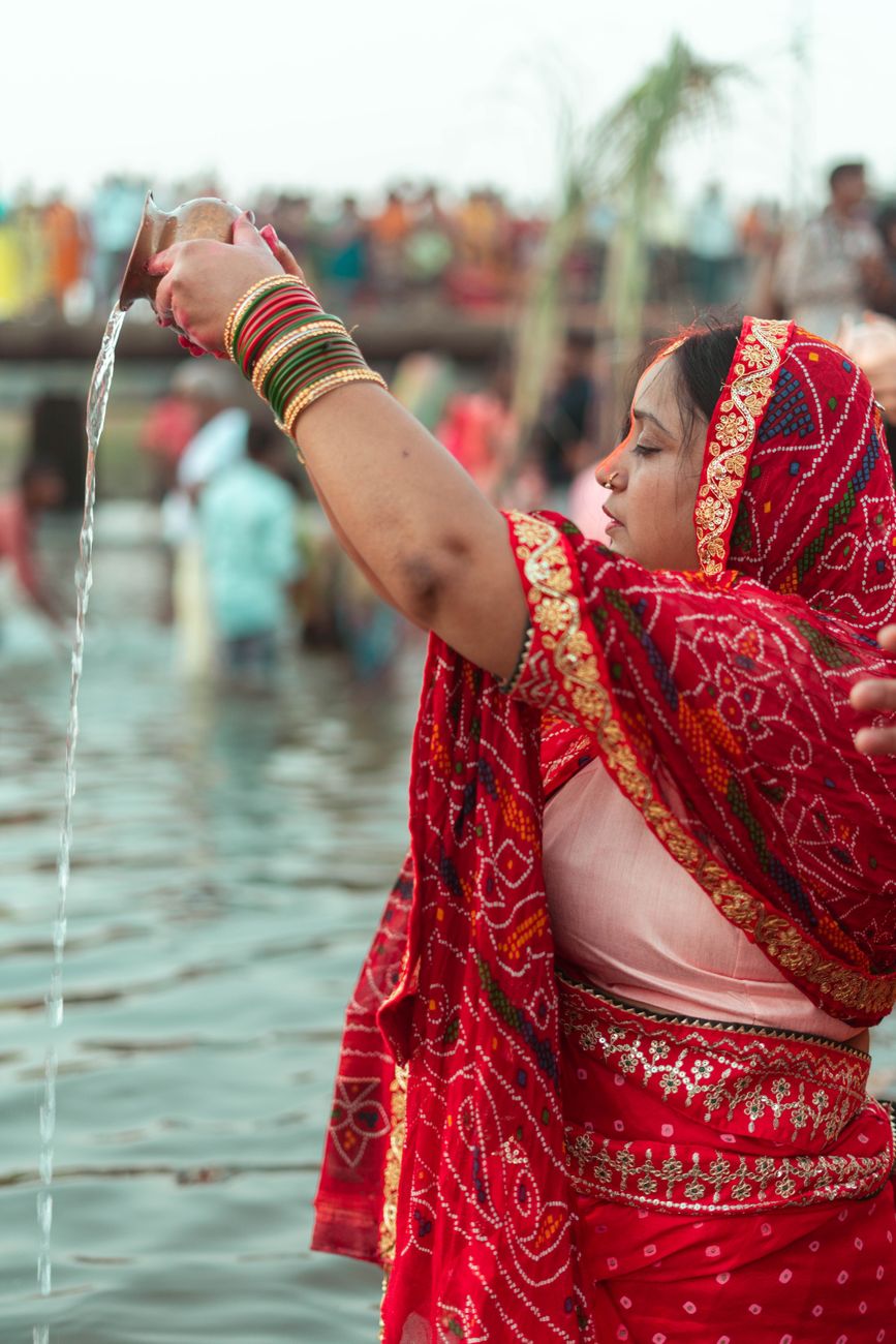 South Asian woman performing a water-pouring ritual during a traditional ceremony.