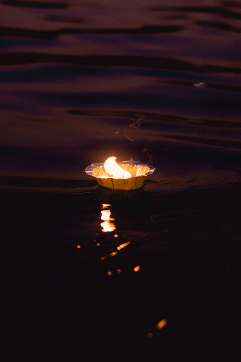 A single floating candle glowing on dark still water