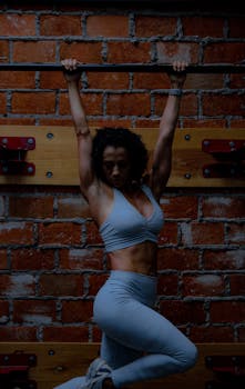 Fit woman in activewear doing exercise on a pull-up bar in an indoor gym setting.
