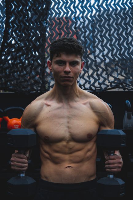 Shirtless man lifting dumbbells, showcasing muscles in a gym setting. Shirtless man lifting dumbbells, showcasing muscles in a gym setting.