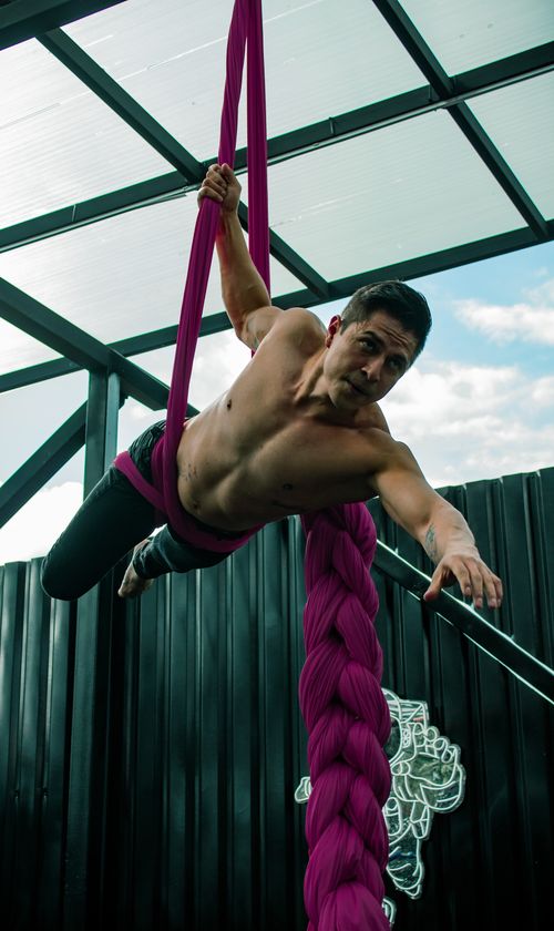 Free Shirtless man performing aerial silk acrobatics in an outdoor setting. Stock Photo