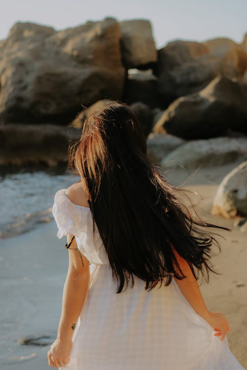 Back View of a Woman in White Dress Standing on the Sea Shore