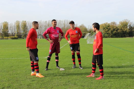 Four soccer players in red and black uniforms strategizing on a green football field.