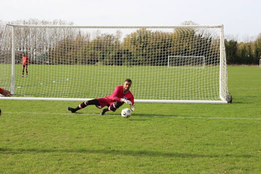 Dynamic scene of a goalkeeper diving to save a goal during a soccer match, showcasing athletic skills.