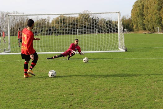 A soccer player prepares to take a shot as the goalkeeper dives to save in an outdoor match.