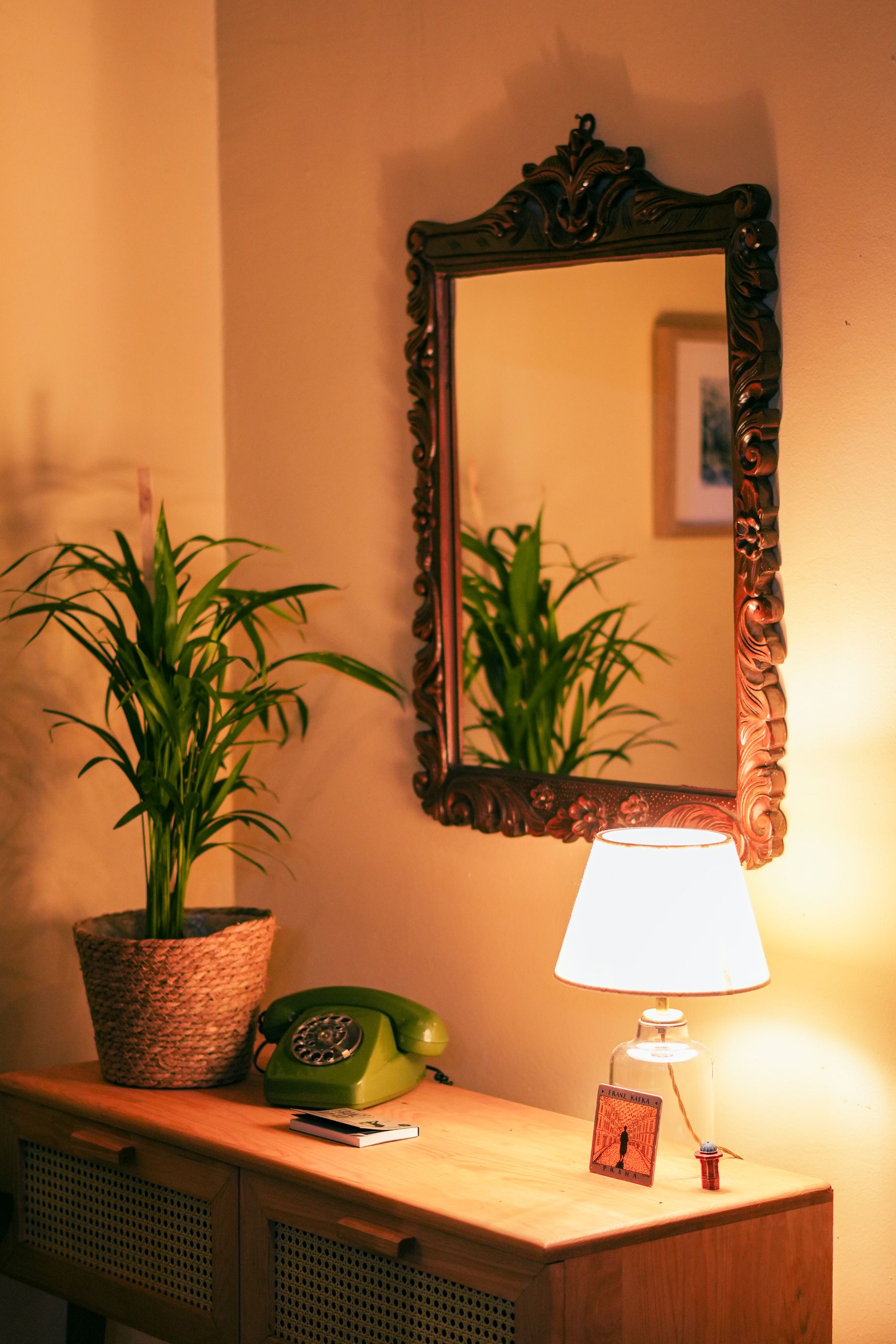 Warm wooden console with a lit table lamp, vintage mirror and plant