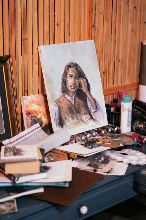 Free An artist's workspace featuring a detailed portrait painting surrounded by art supplies. Stock Photo