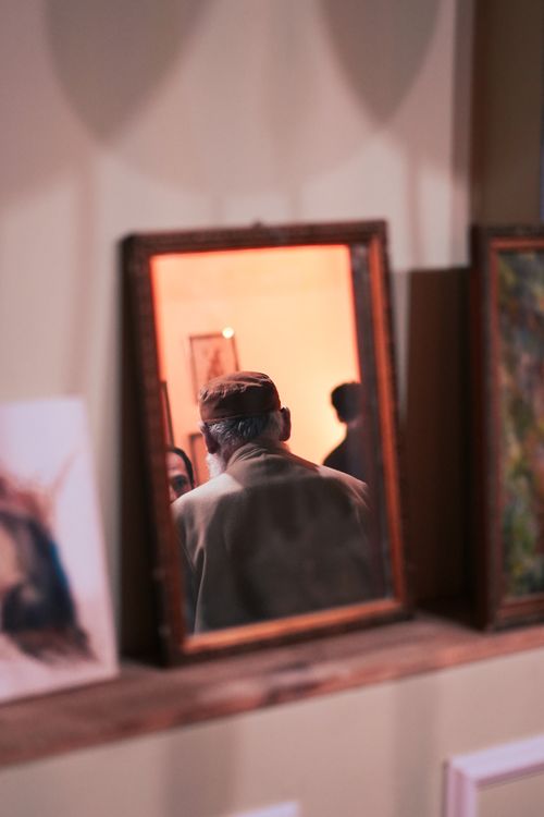 Free A thoughtful reflection of a man in an art gallery mirror, surrounded by paintings. Stock Photo