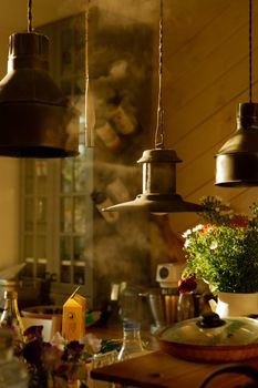 A warm, vintage-style kitchen scene with hanging lamps and flowers on the counter.
