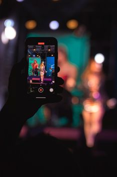 Silhouette of a hand recording a live concert on a smartphone at night in Adana, Turkey.