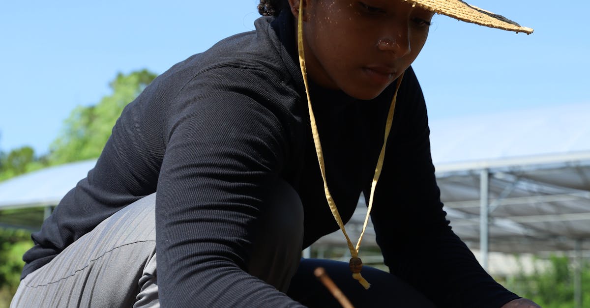 Photo by Joice Rivas A woman in a straw hat planting seeds in a rural field on a sunny day.