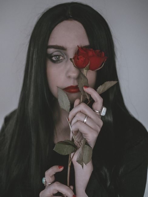 Moody portrait of a woman holding a red rose against a muted background, perfect for gothic themes.