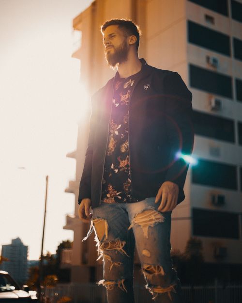 Free Stylish bearded man in ripped jeans and black jacket in urban sunlight. Stock Photo