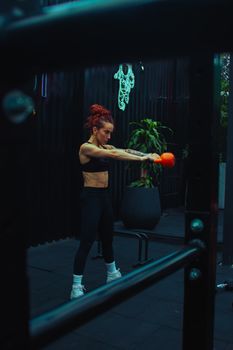 Focused woman performs kettlebell swing in an indoor gym setting, showcasing strength and fitness.