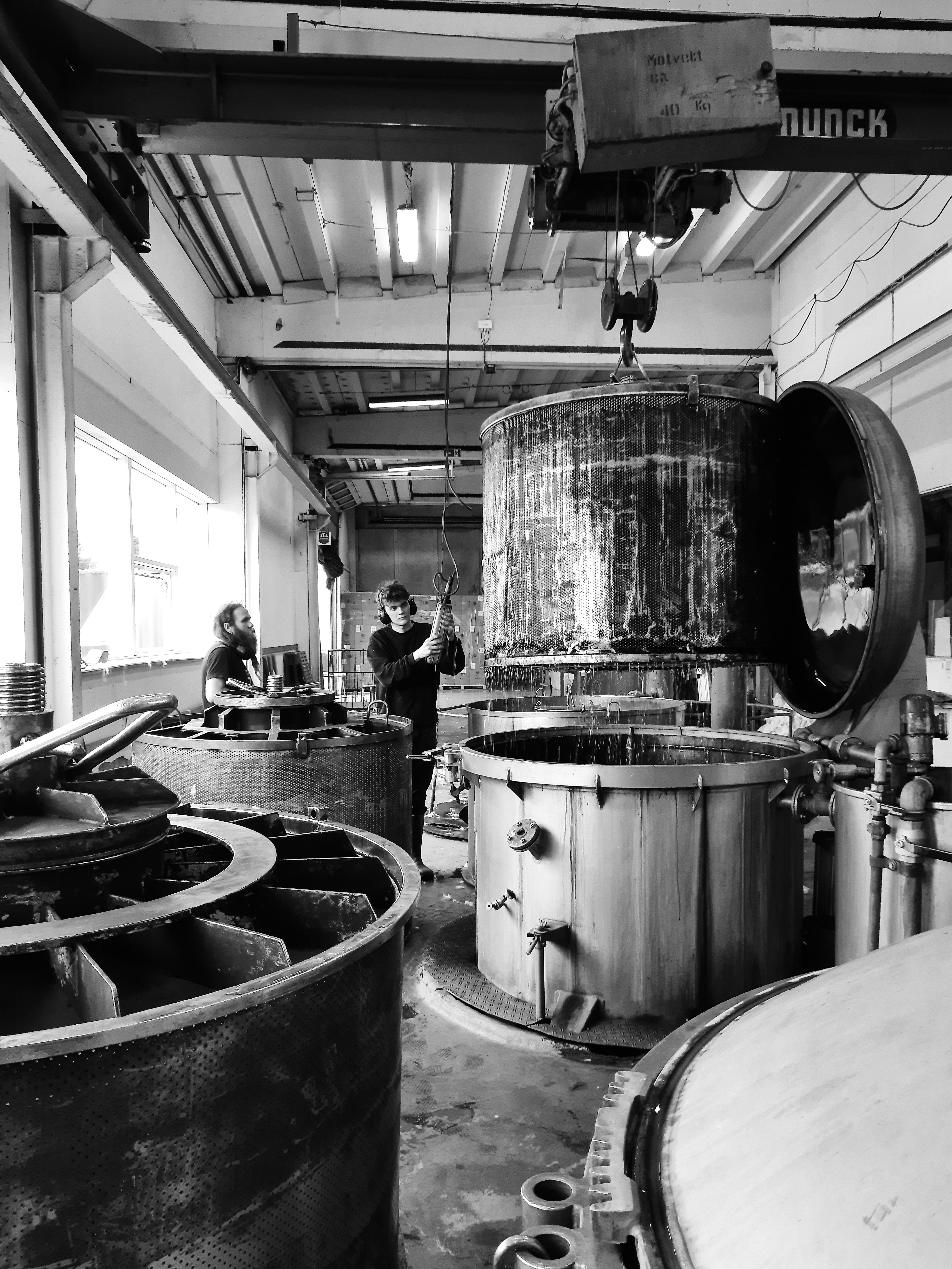 Black and white image of a brewery interior with industrial equipment and workers.