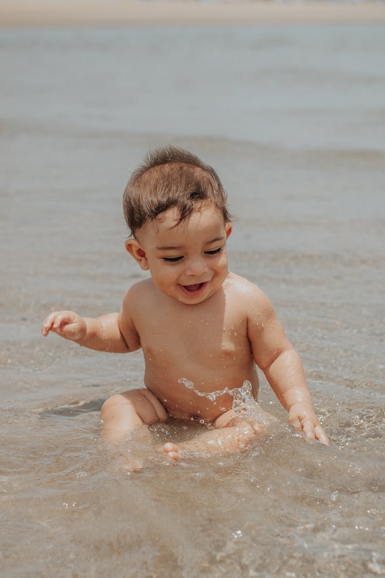 Cute Smiling Baby Sitting In Sea