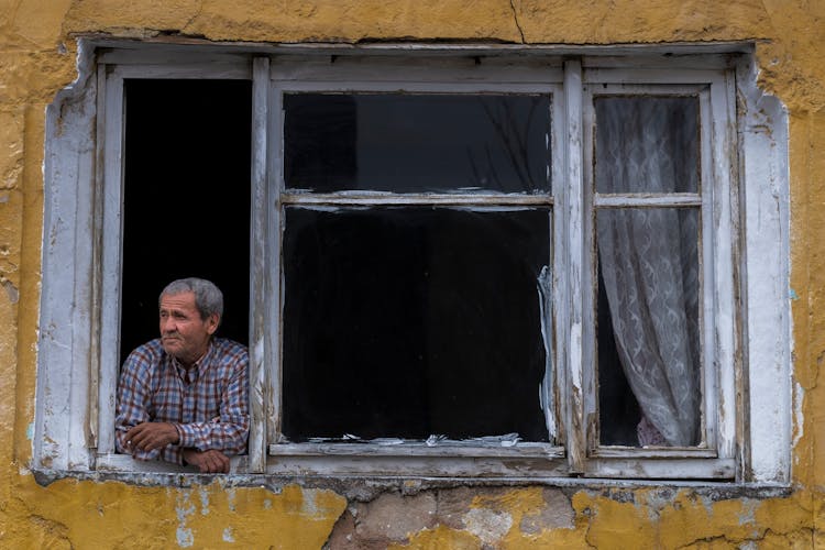 Elderly Man Looking Out The Window In An Old Building 