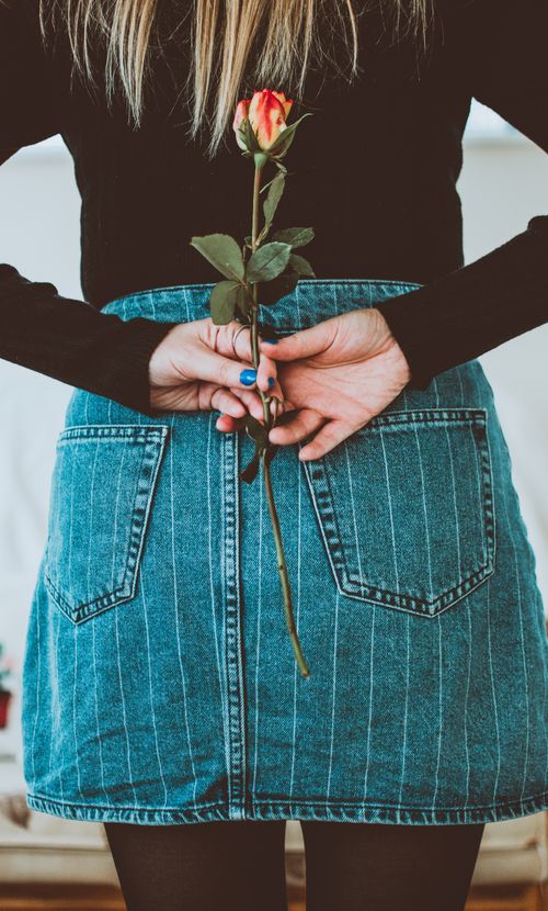 Free Stylish woman in denim skirt holding a rose behind her back, showcasing casual fashion. Stock Photo