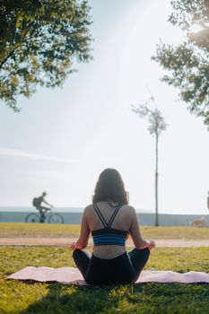 Back view of a woman practicing yoga in a sunny park, embracing a healthy lifestyle.