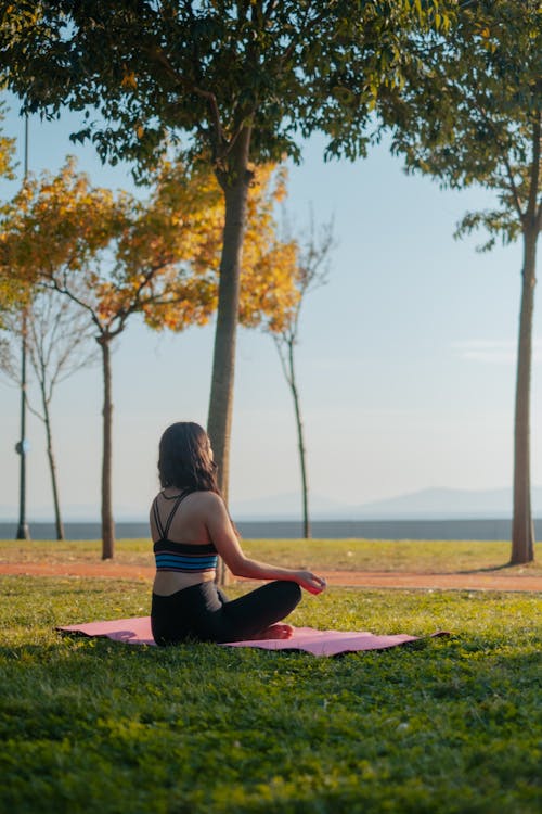 A Woman Sitting on Yoga Mat Near the Green Trees