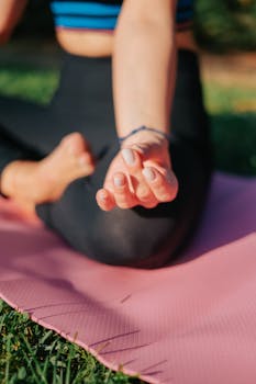 Close-up of a woman meditating in the lotus position on a pink yoga mat outdoors.