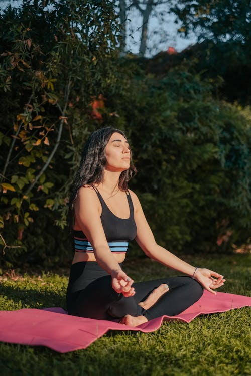 A Woman in Black Leggings Sitting on Yoga Mat while Meditating with Her Eyes Closed