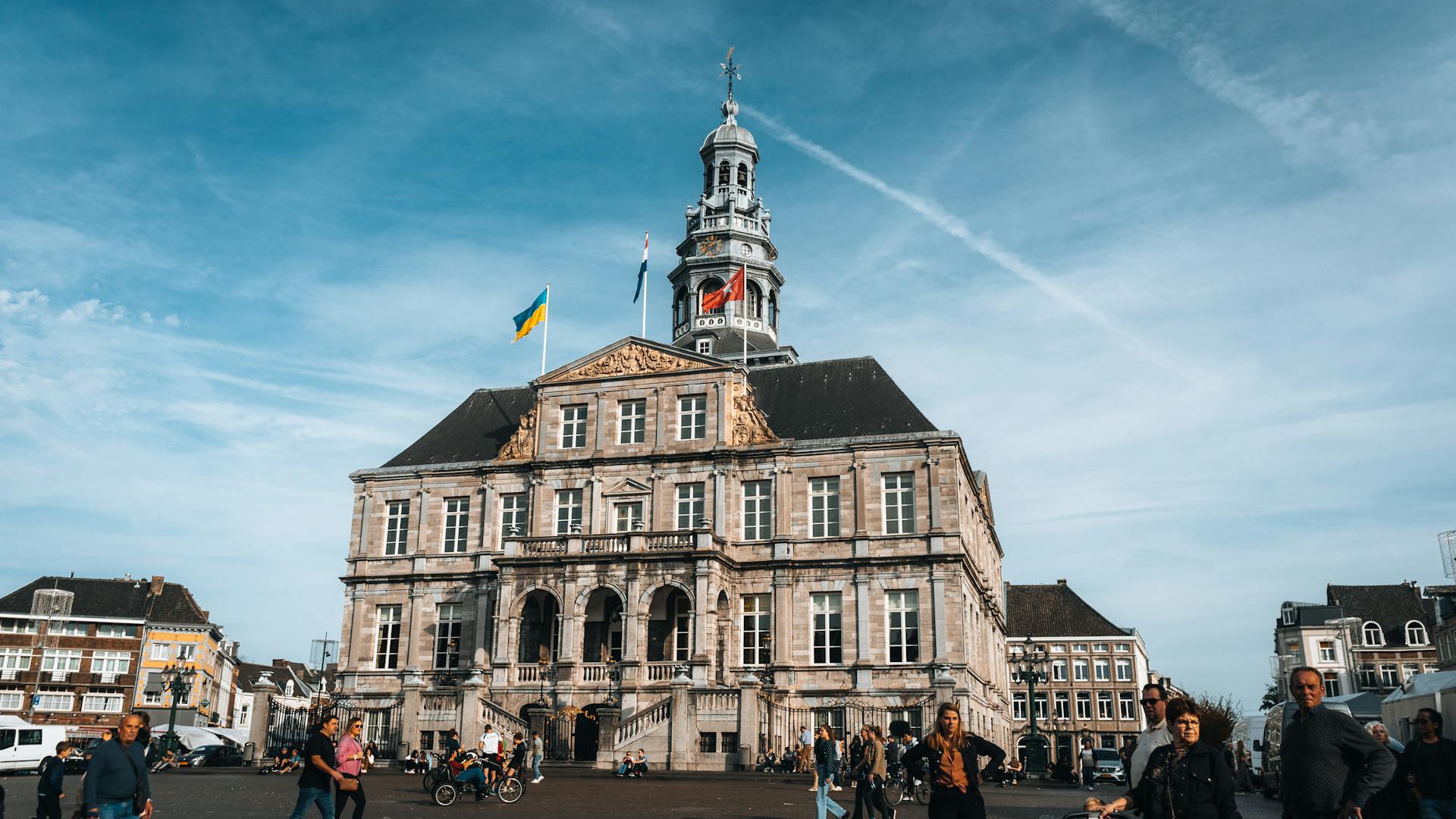 A bustling scene at Maastricht City Hall with people walking under a clear blue sky.