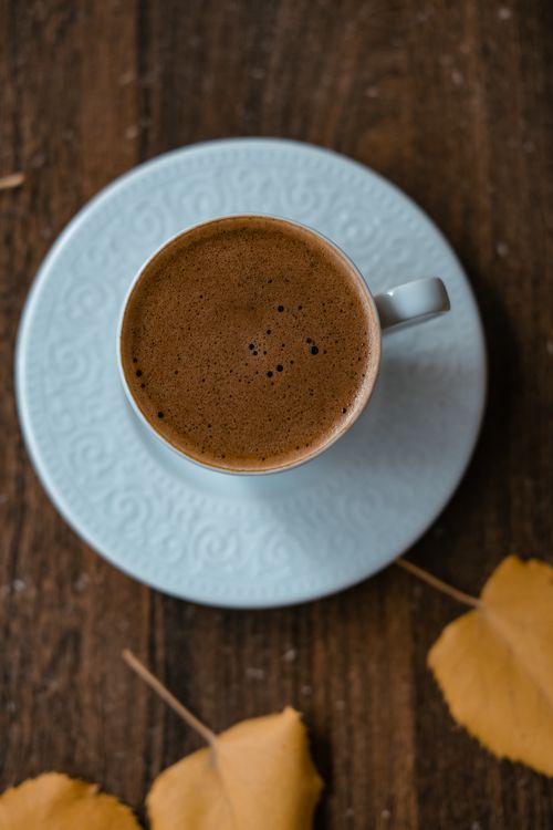 Free Overhead view of a hot coffee cup on a blue plate, surrounded by autumn leaves on a wooden table. Stock Photo