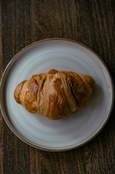 A crisp, golden-brown croissant displayed on a ceramic plate, perfect for breakfast imagery.