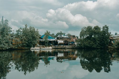 Free Peaceful view of rustic houses by a reflective lake under cloudy skies, capturing nature's tranquility. Stock Photo