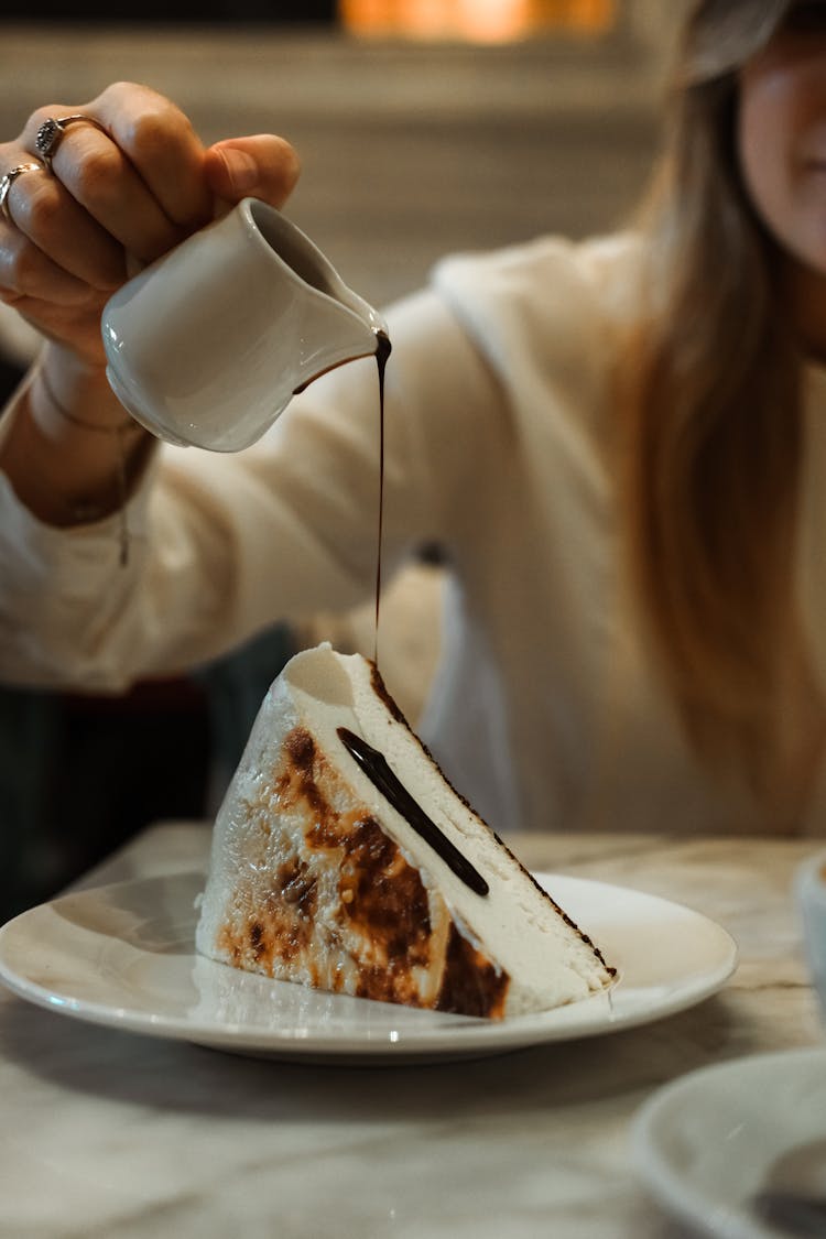 A Person Pouring Chocolate Syrup On The Cake