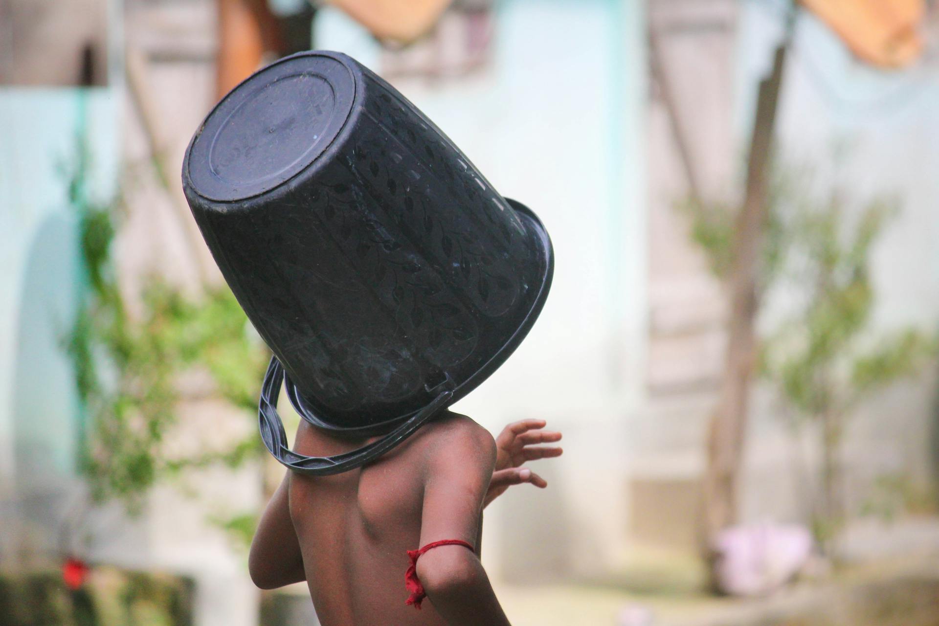 A child playing outdoors with a bucket covering their head, showcasing fun and imagination.