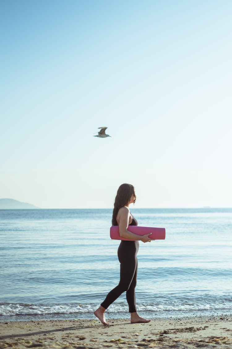 Woman Walking With Mat On Beach