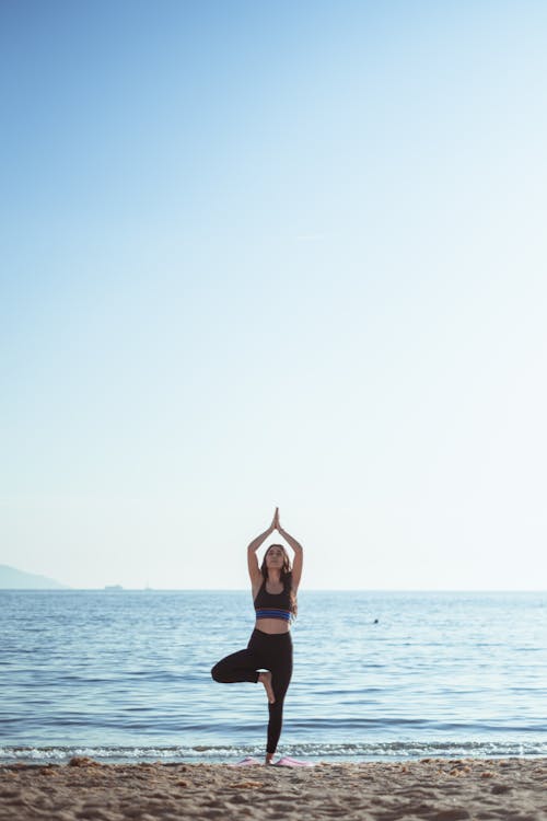 Woman Practicing Yoga on Sea Shore under Clear Sky