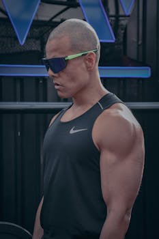 Athletic bald man in a black tank top and sunglasses indoors, showcasing physical fitness.