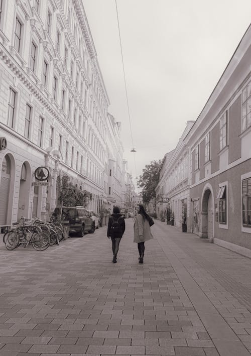 A Grayscale Photo of People Walking on the Street Between Buildings