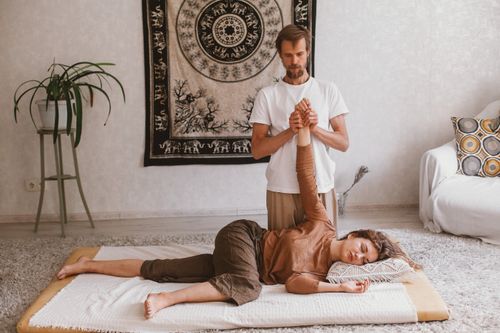 Free A man performs a massage on a woman lying on a carpet, both at ease in a serene indoor setting. Stock Photo