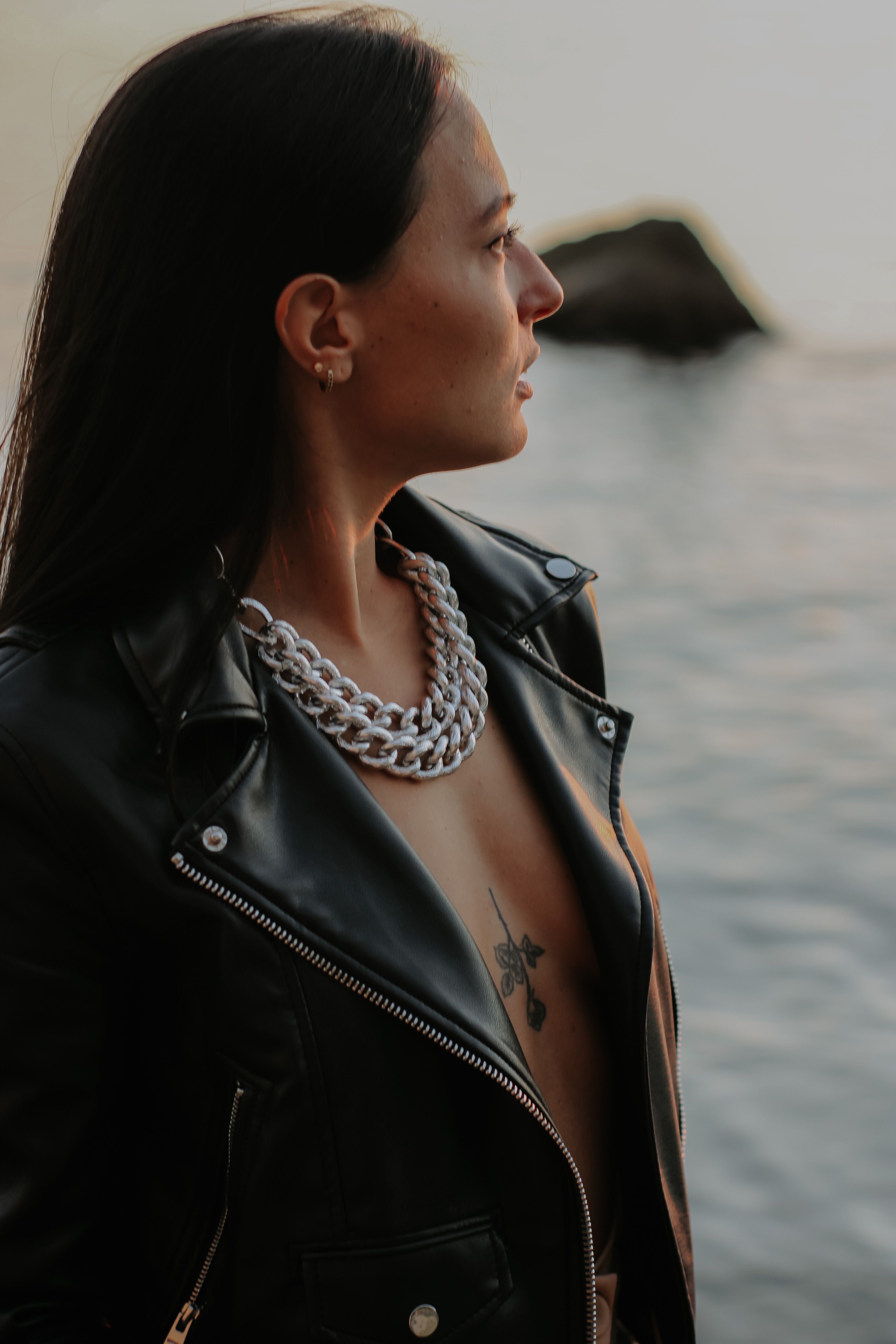 Side view portrait of a woman in a leather jacket with tattoos by the water.
