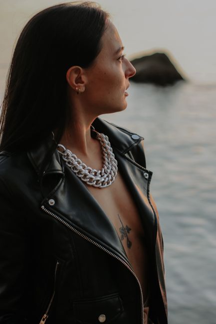 Side view portrait of a woman in a leather jacket with tattoos by the water.